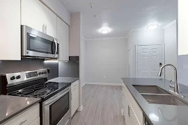 Modern apartment kitchen with stainless steel appliances and light wood flooring.