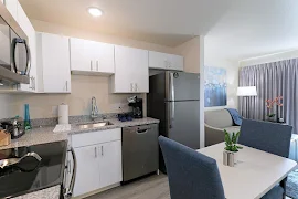 Model kitchen with stainless steel appliances, white cabinets, stone countertops, and small seating table with a plant