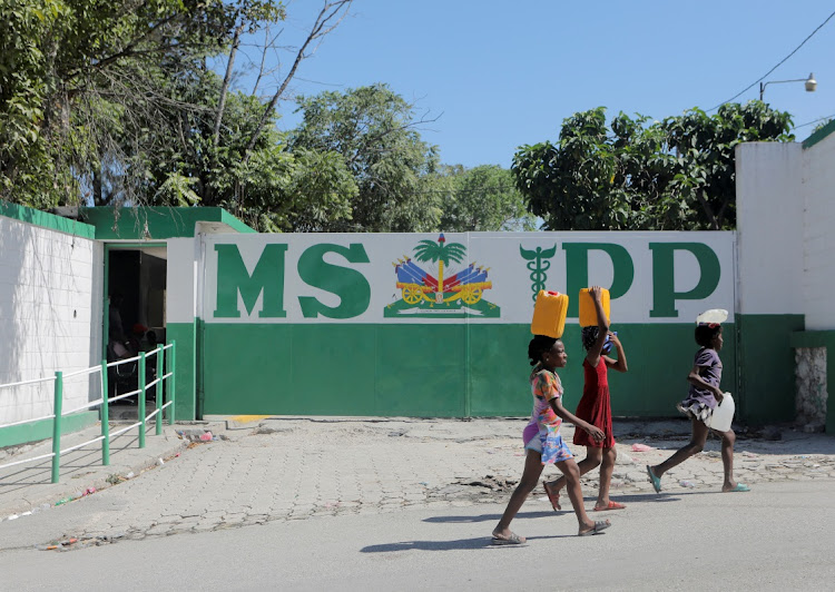 Young girls carry water containers while walking past an office of the Ministry of Public Health and Population (MSPP), in Port-au-Prince, Haiti October 4, 2022.