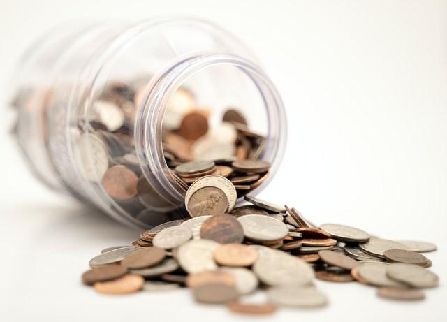 A clear jar with spilled coins. 