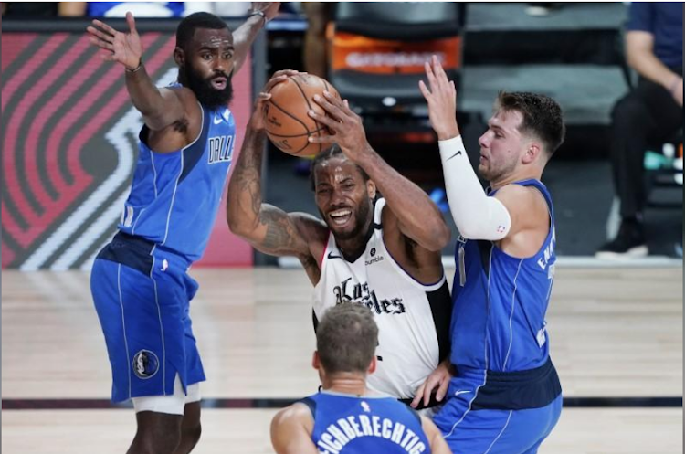 Los Angeles Clippers' Kawhi Leonard, center, is pressured by Dallas Mavericks' Luka Doncic (R)