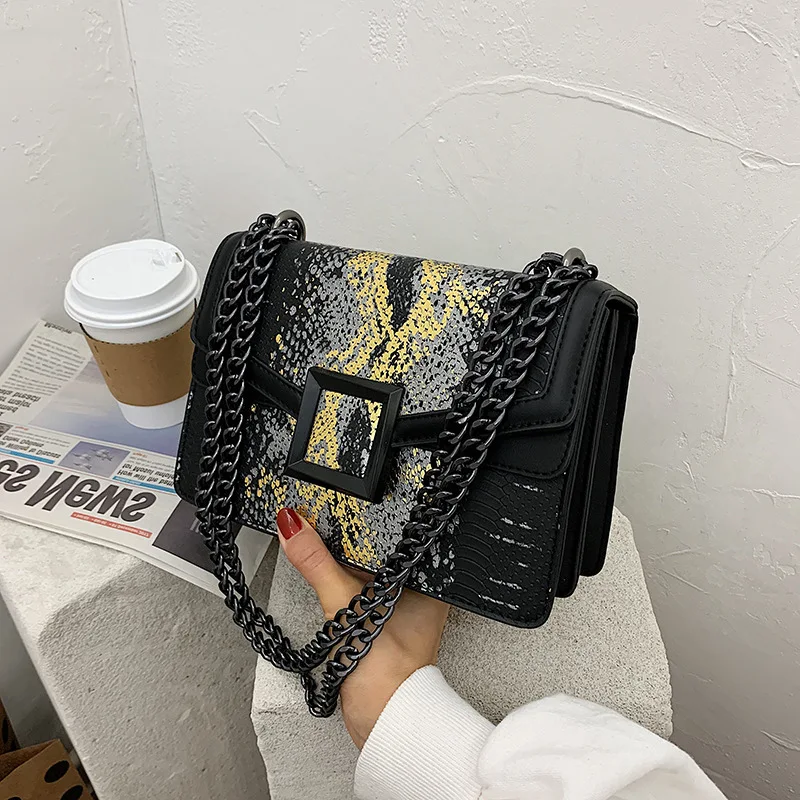 Sac bandoulière tendance à imprimé serpent et chaîne, porté à une épaule. Un sac moderne pour un look stylé et élégant, parfait pour toutes occasions.
