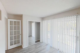 Bedroom with wood plank flooring, mirror, and sliding patio door with vertical blinds