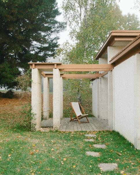 Exterior of concrete house with wooden details and pillars near green lawn with stone steps