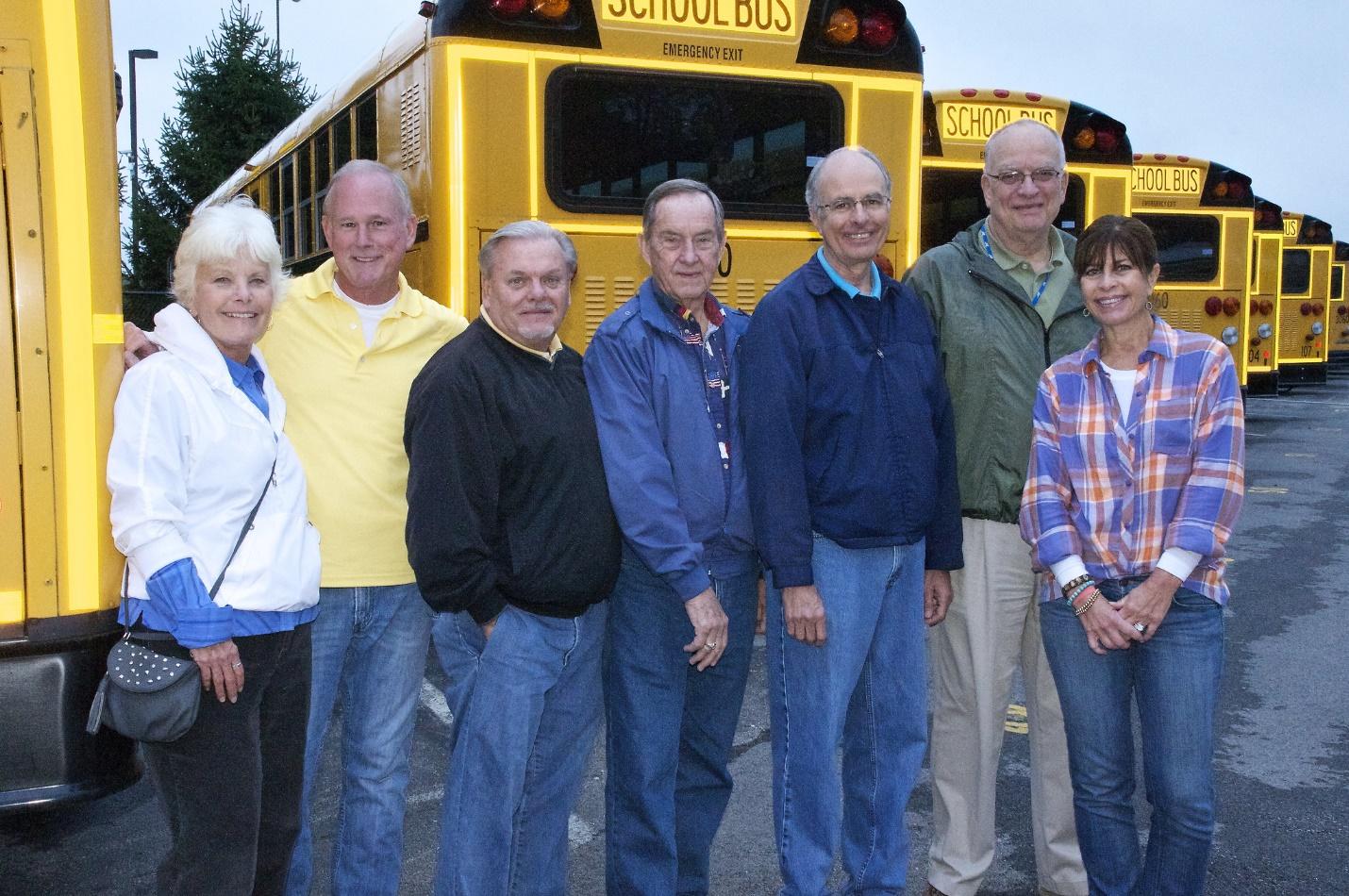 A group of people posing for a photo in front of a yellow school bus

Description automatically generated