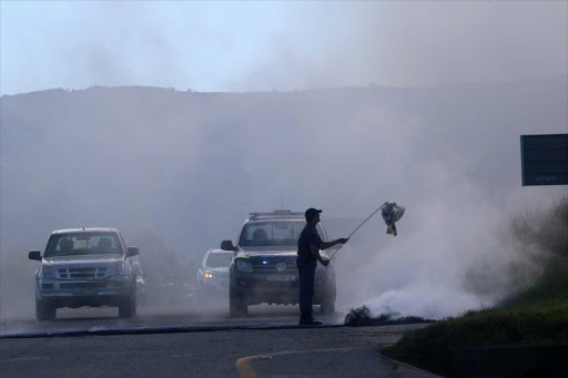 AFTERMATH: A police officer seen trying to clear the debris on the road that leads into Stutterheim following the protests in the Amahlathi municipality Picture: MICHAEL PINYANA