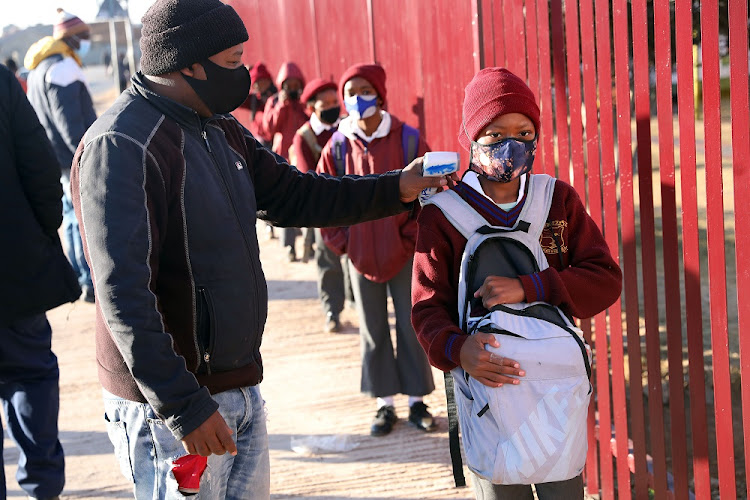 School children wearing masks get their hands sanitised and temperatures checked as they arrive at Mayibuye Primary School, Snake Park in Soweto on July 26 2021.