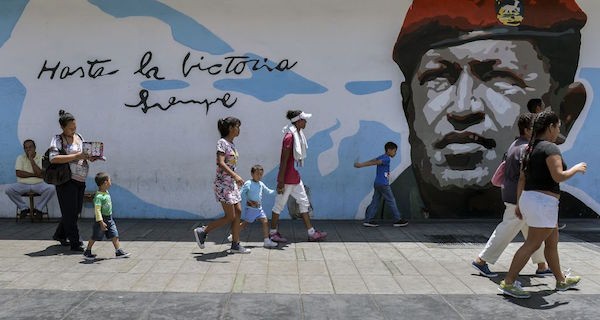 TOPSHOT - People walks by a graffiti with an image of late President Hugo Chavez in Caracas on May 11, 2018. - Venezuelan citizens will face presidential elections on May 20 amid a severe socio-economic crisis, with hyperinflation - estimated at 13,800% by the IMF for 2018 - and shortages of food, medicines and other basic products. (Photo by Luis ROBAYO / AFP) (Photo credit should read LUIS ROBAYO/AFP/Getty Images)