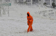 A Capetonian walks in ocean foam at Sea Point in Cape Town as strong winds and high seas lashed the promenade on July 13 2020.