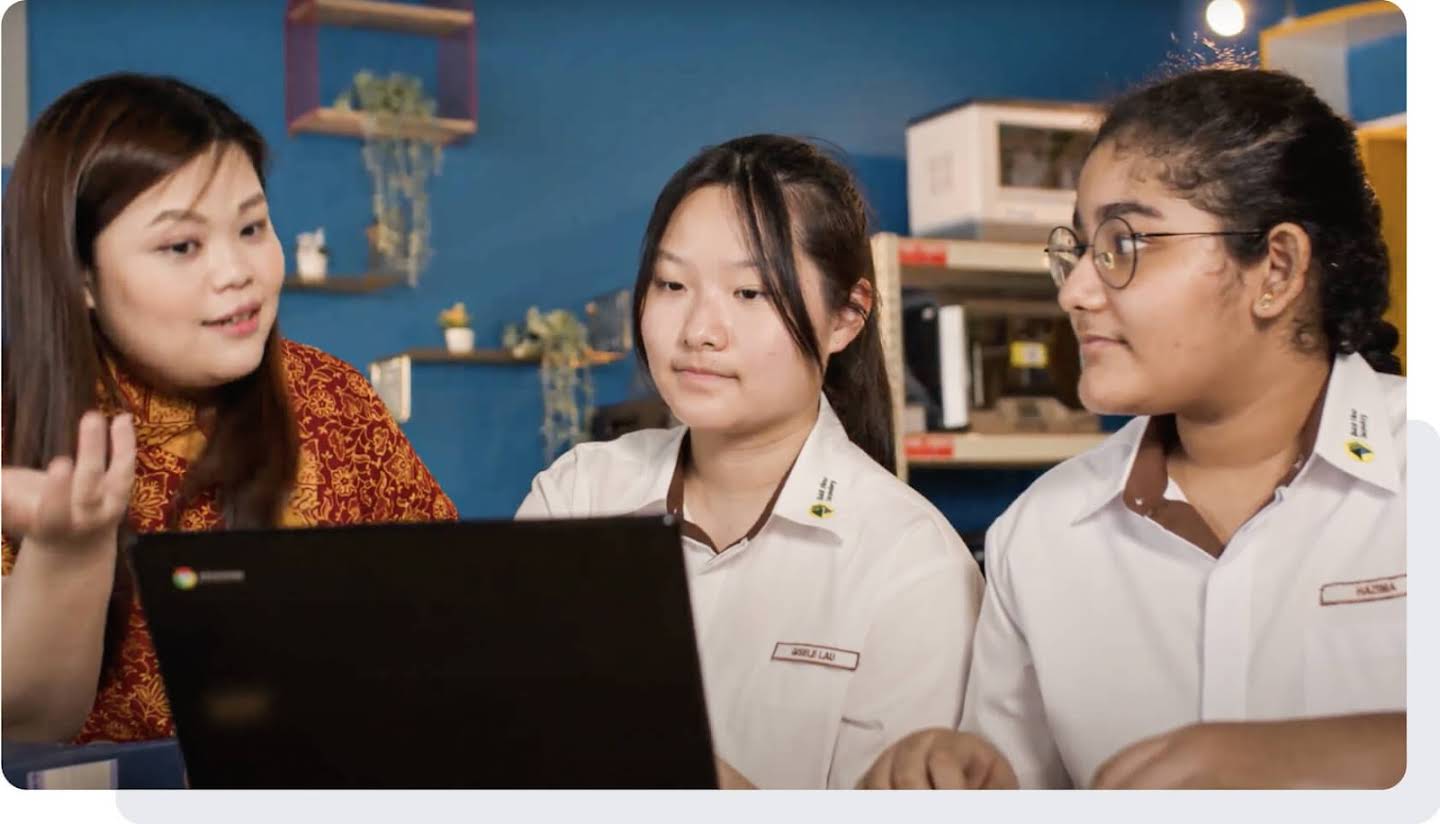 Seorang guru perempuan dan dua orang pelajar sedang menggunakan Chromebook di dalam bilik darjah.