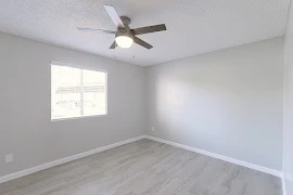 Bedroom with wood-inspired flooring, light grey walls, white trim and a ceiling fan with light. 