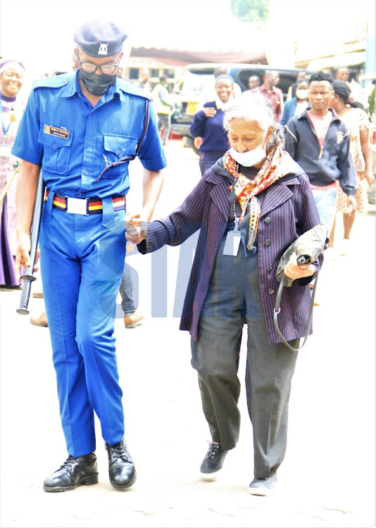 A policeman assists an old woman after viewing the body of the late retired president Mwai Kibaki in parliament on April 26, 2022.