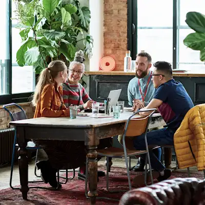 Cuatro compañeros de trabajo reunidos en una mesa de reuniones de una oficina con plantas.