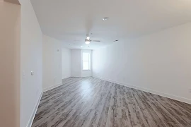 Open living room with white walls, a ceiling fan, window, and wood finish flooring