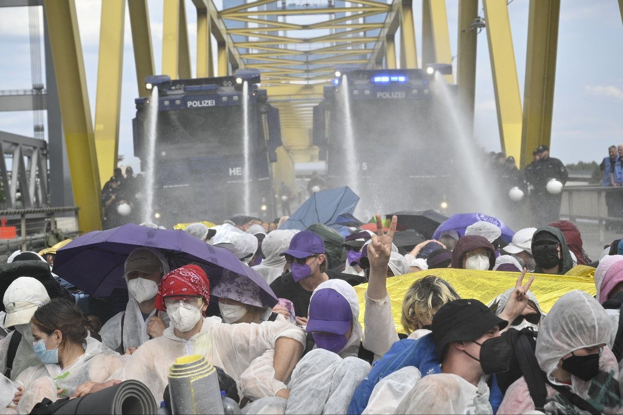 water cannons mounted on trucks blast sitting protesters on a bridge