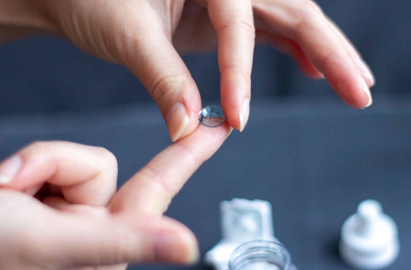 A close-up of human hands with an Ortho-k contact lens on the tip of a finger.