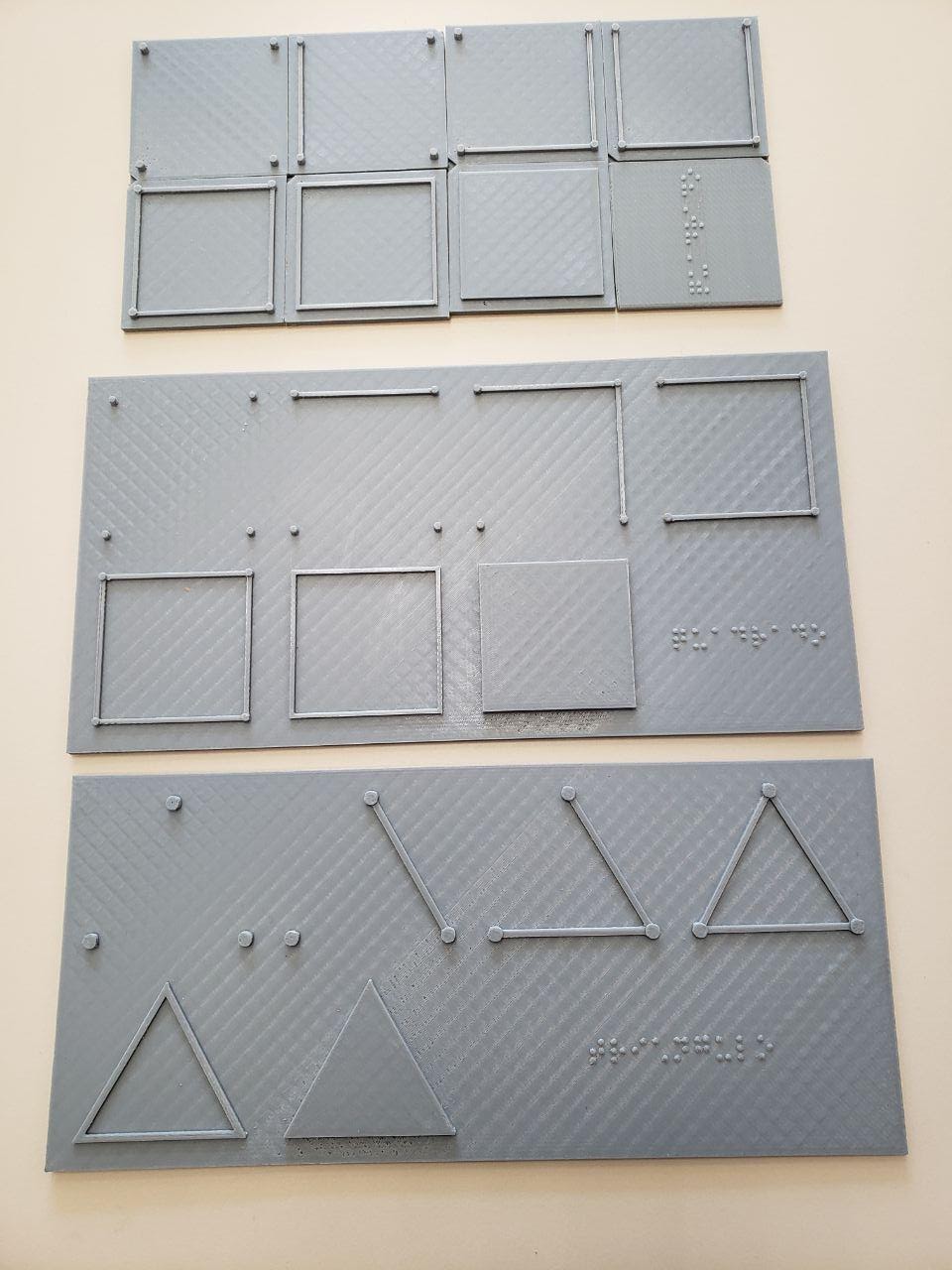 Duas chapas cinzas impressas em 3D representando a formação de formas geométricas, e oito peças soltas também representando a formação de formas geométricas.