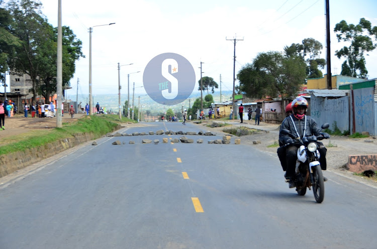 A motorbike rider and his passenger pass by a roadblock along the Eveready - Kaptembwa road in Nakuru on July 12, 2023.