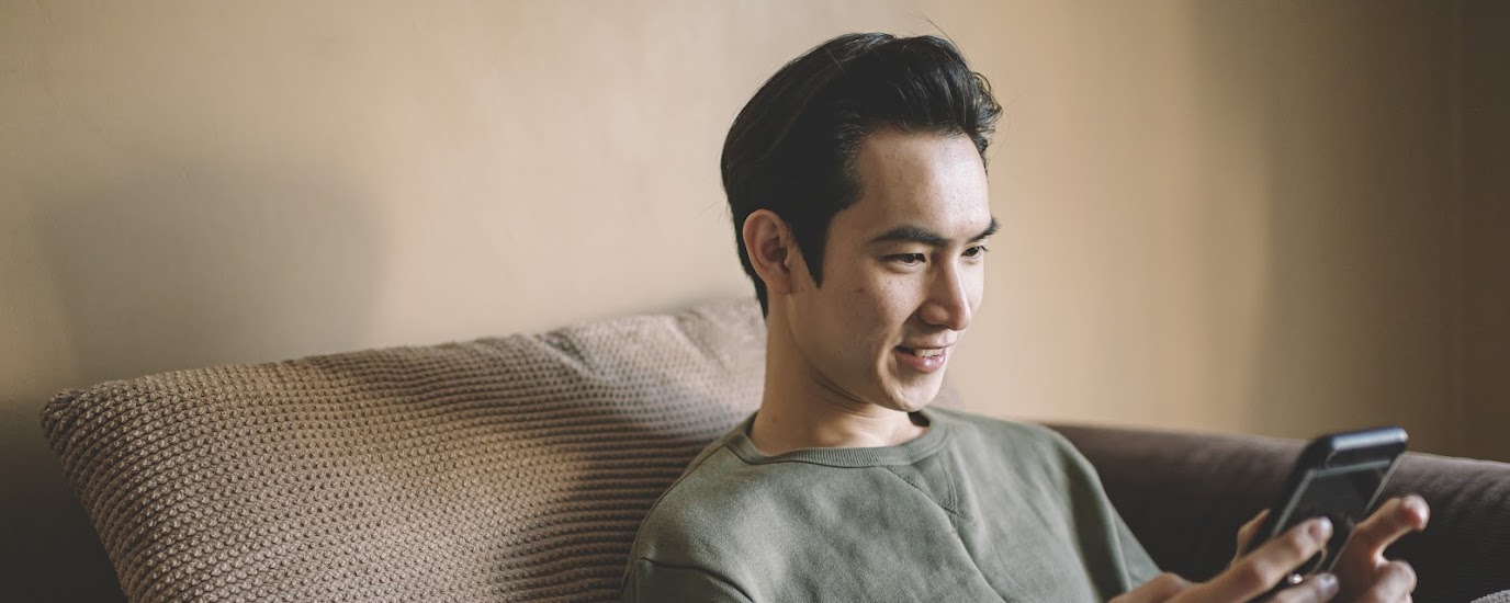 Young man sits on couch looking at cell phone