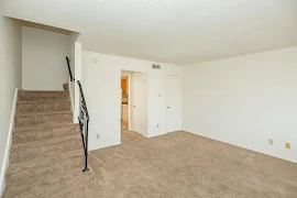 Living room area with neutral carpet, view of stairwell with metal banister, white walls and trim