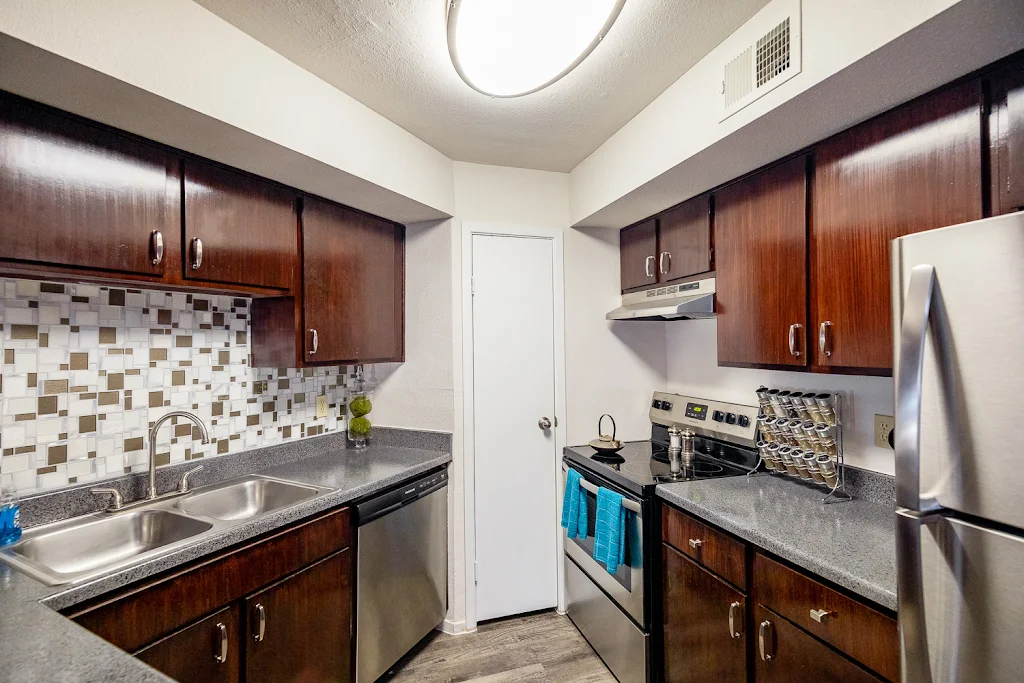 Kitchen with dark wood cabinets, tile backsplash, gray speckled countertop, and stainless steel appliances