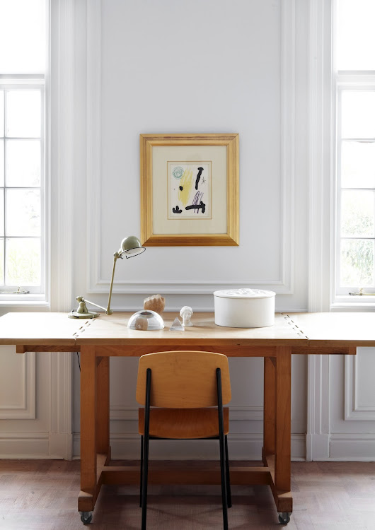 Various items are displayed on the wooden table in the bedroom, including a Jielde lamp. In front of it is a Standard Chair by Jean Prouvé. The artwork is by Catalan artist Joan Miró.