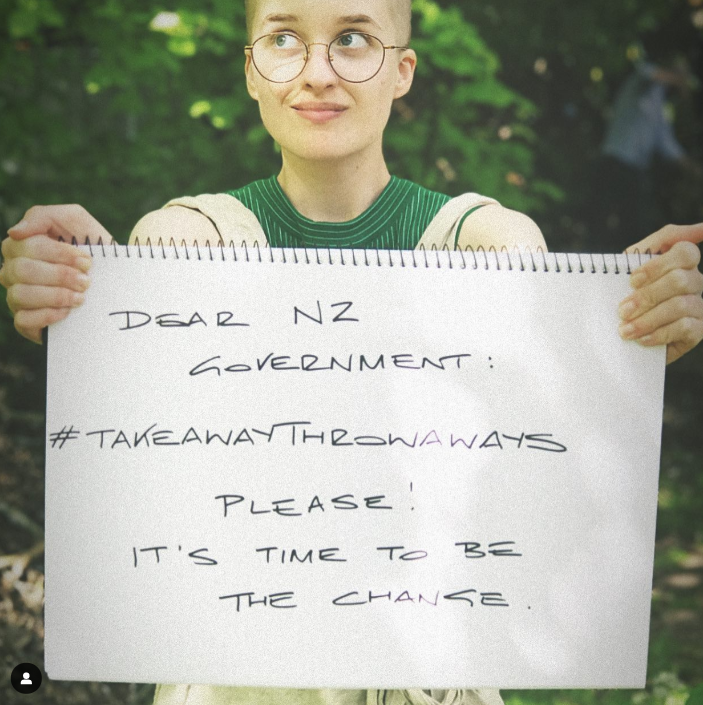 A person in green holds a handwritten sign: Dear NZ Government #TakeawayThrowaways please! It's time to be the change