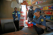 Police officers searching a spaza shop in Diepsloot, confiscating cigarettes and cigarette papers.