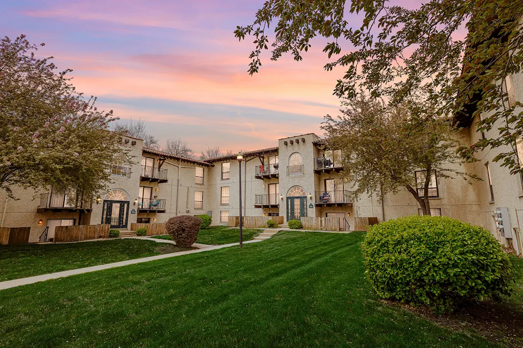 Delrado Apartments two story apartment building with trees and green space surrounding at dusk