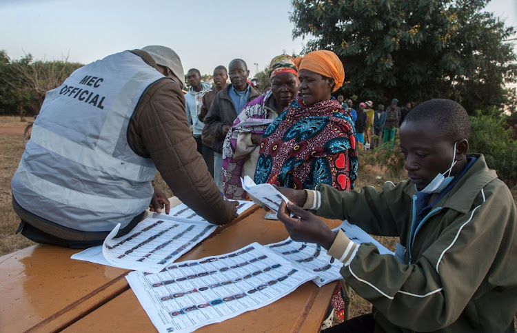 Electoral officials check the voters roll while people queue to vote at the Malembo polling station during the presidential elections in Lilongwe on June 23, 2020.