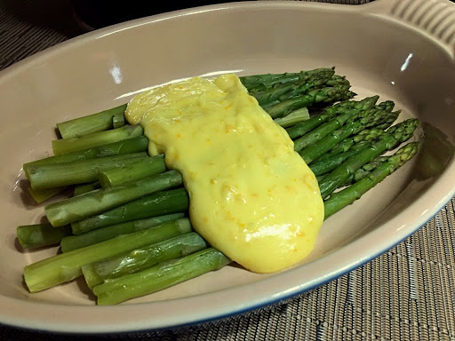 A bunch of asparagus sitting on a serving dish with a sauce on top.