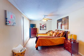 Model bedroom with plush carpet, decorative bedspread and pillows, TV and a large window