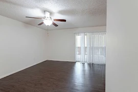 Living room with dark wood inspired flooring, sliding doors with vertical blinds, five blade ceiling fan