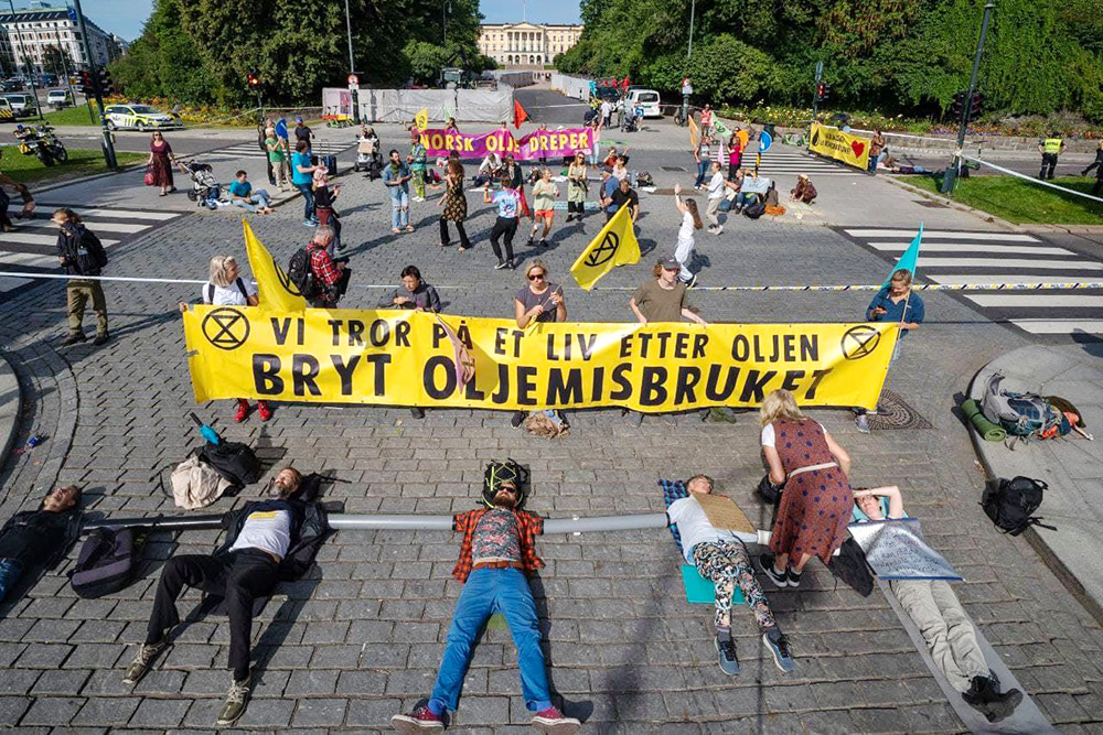 Dozens of rebels blockade a large crossroads. Some dance, some hold banners, some lie on the road connected by arm tubes.