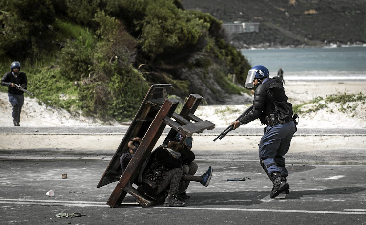 A policeman moves around a barricade after shooting Ona Dubula in the face with rubber bullets as police moved in to clear away protesters in Hout Bay.