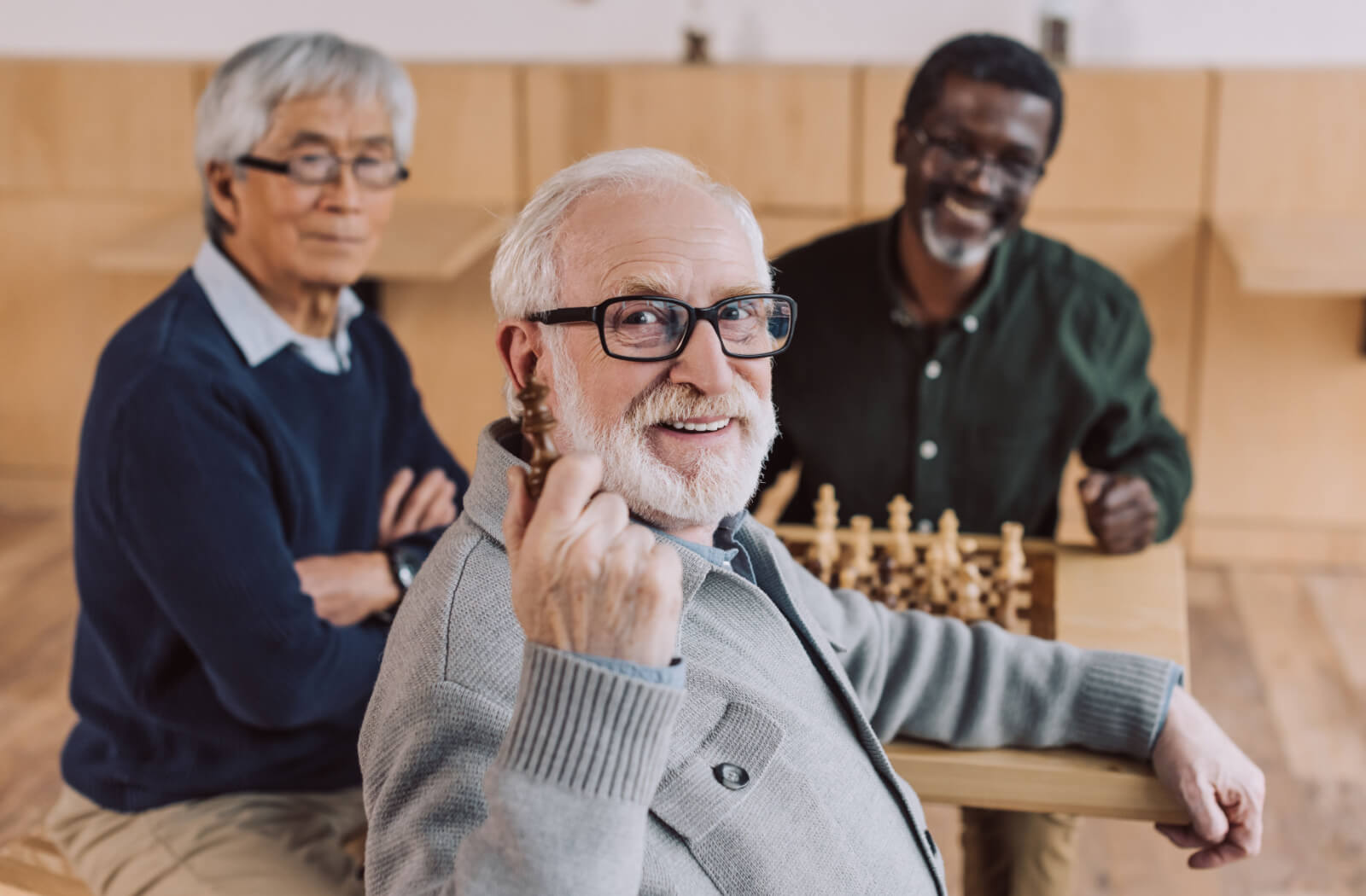 Three senior men sitting next to each other at a table playing a game of chess