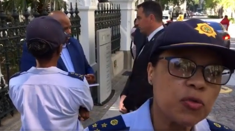 A high ranking police officer approaches, moments before the cellphone held by a journalist at parliament was slapped away.