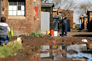 A man warns a toddler to be careful as he walks  past a spot flooded at the Actonville hostel in Benoni, Ekurhuleni. The hostel has raw sewage overflowing into the walkways and hasn't seen basic service delivery in weeks. 