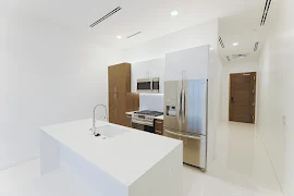 Kitchen with large white stone island, stainless steel appliances, white and brown cabinets, and recessed lighting