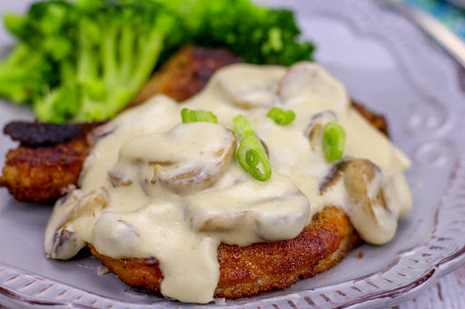 Pork chops with mushroom sauce on a plate with green onions sprinkled on top.