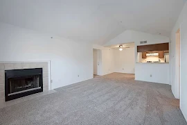 Living room with large fireplace, neutral carpet, & vaulted ceilings. Living room flows into the dining room and kitchen