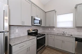 Back wall of kitchen includes refrigerator to the left of the oven and overhead microwave. Kitchen sink on adjacent wall