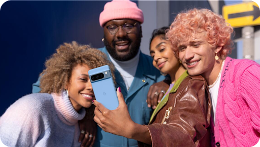 A group of people taking a selfie with a blue Pixel 8 Pro phone.