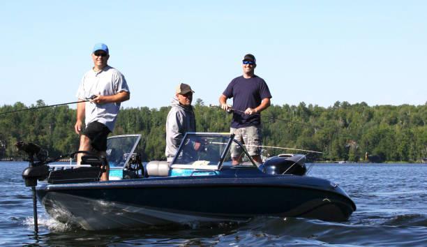 Three men in a blue boat, fishing 2. Three middle aged men are enjoying a sunny day out on the water fishing.  The water is a freshwater lake in the western part of the Great Lakes region of the United States. group fishing stock pictures, royalty-free photos & images