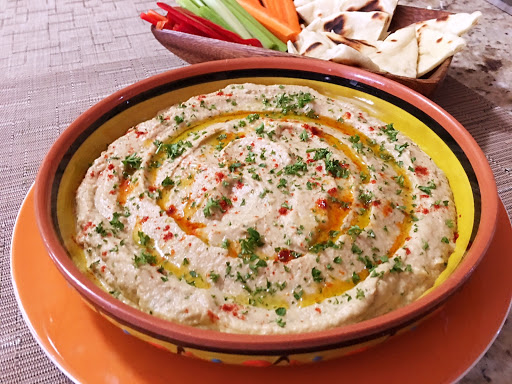 Baba Ghanoush in a serving dish sitting on a white/orange plate with crudites in the background.