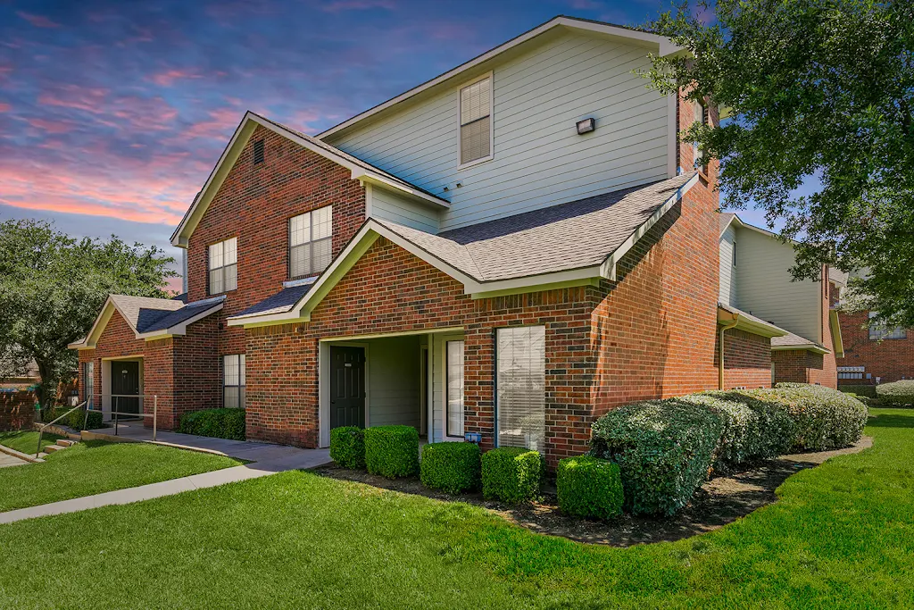 Apartment building exterior with brick and beige siding and surrounded by grass and bushes