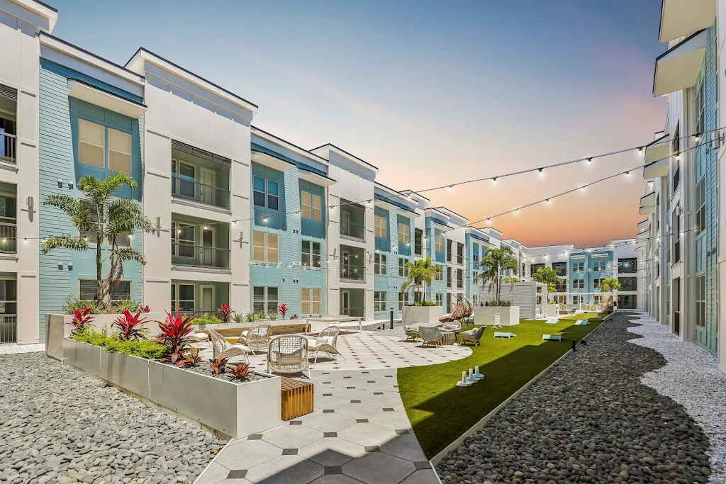 View of community courtyard featuring a lot of seating and strung lights with apartment buildings in the background at dusk