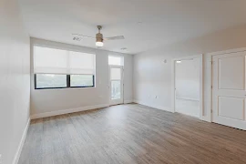 Living room with wood-inspired flooring, light walls and trim, ceiling fan, window with blinds, & exterior door to the porch