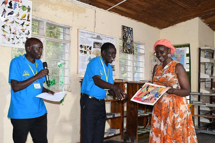 Kisumu First Lady Dorothy Nyong'o receives a gift from Kenya National Visuals and Artists Association Western region coordinator Hosea Otulia and Kiwimbi Library founder Olubayi Olubayi.