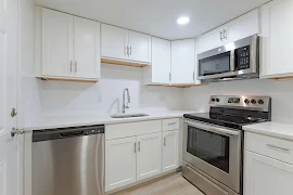 Modern apartment kitchen with stainless steel appliances, white cabinetry, and light countertops.